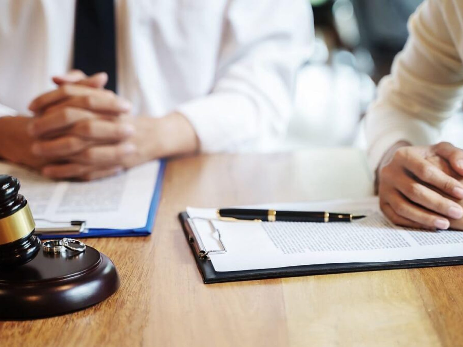 Two people sit at a table with official documents, a hammer and gavel, and two rings.