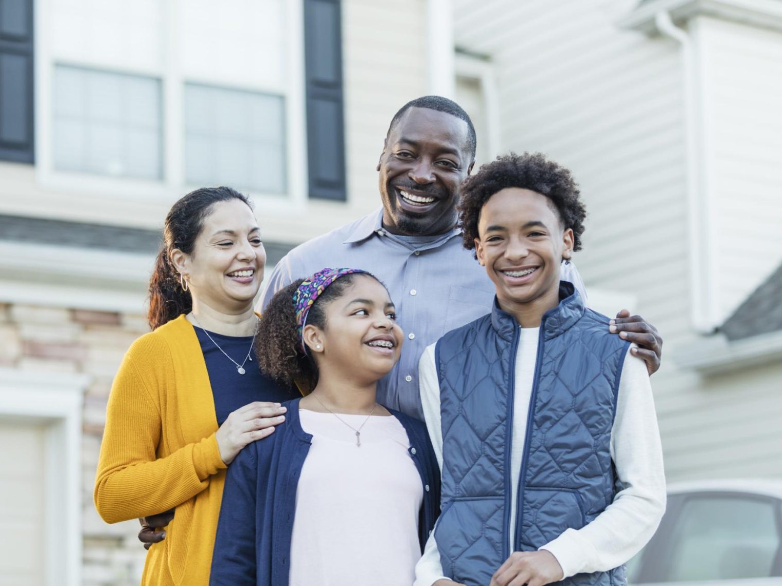 An African American family standing outside the new home they just bought.