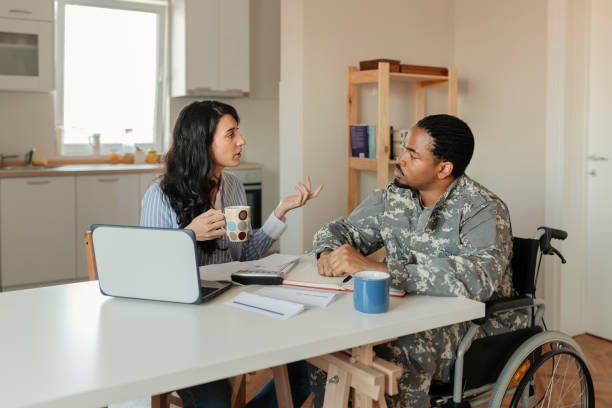 Woman and man in army uniform talking at kitchen table while drinking out of mugs