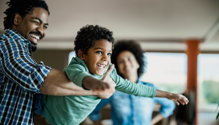 Father holding his son in the air while his wife stands behind them.