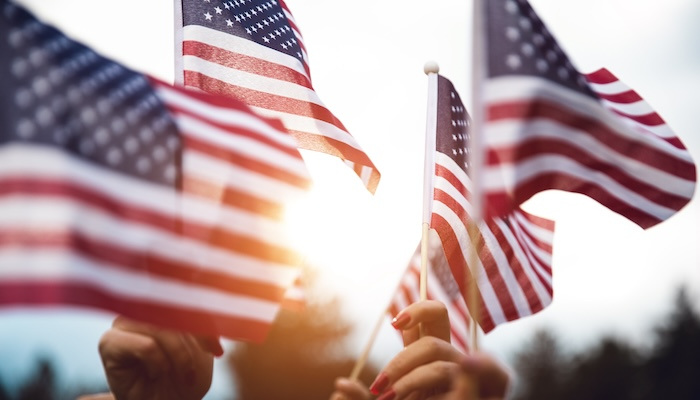 Group of hands waving small American flags in the air.