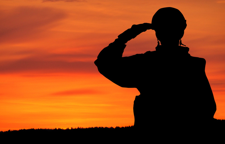 The silhouette of a soldier saluting against a vibrant sunset sky.